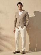 Man wearing a beige cardigan over a white shirt with white pants against a beige background