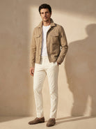 Man wearing a beige jacket, white shirt, and white pants against a beige wall.
