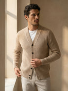 Man wearing a beige cardigan over a white shirt in a softly lit room.