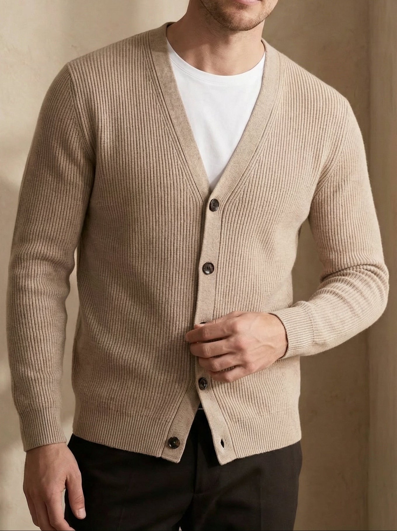 Man wearing a beige cardigan over a white shirt with a neutral background