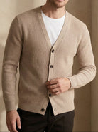 Man wearing a beige cardigan over a white shirt with a neutral background