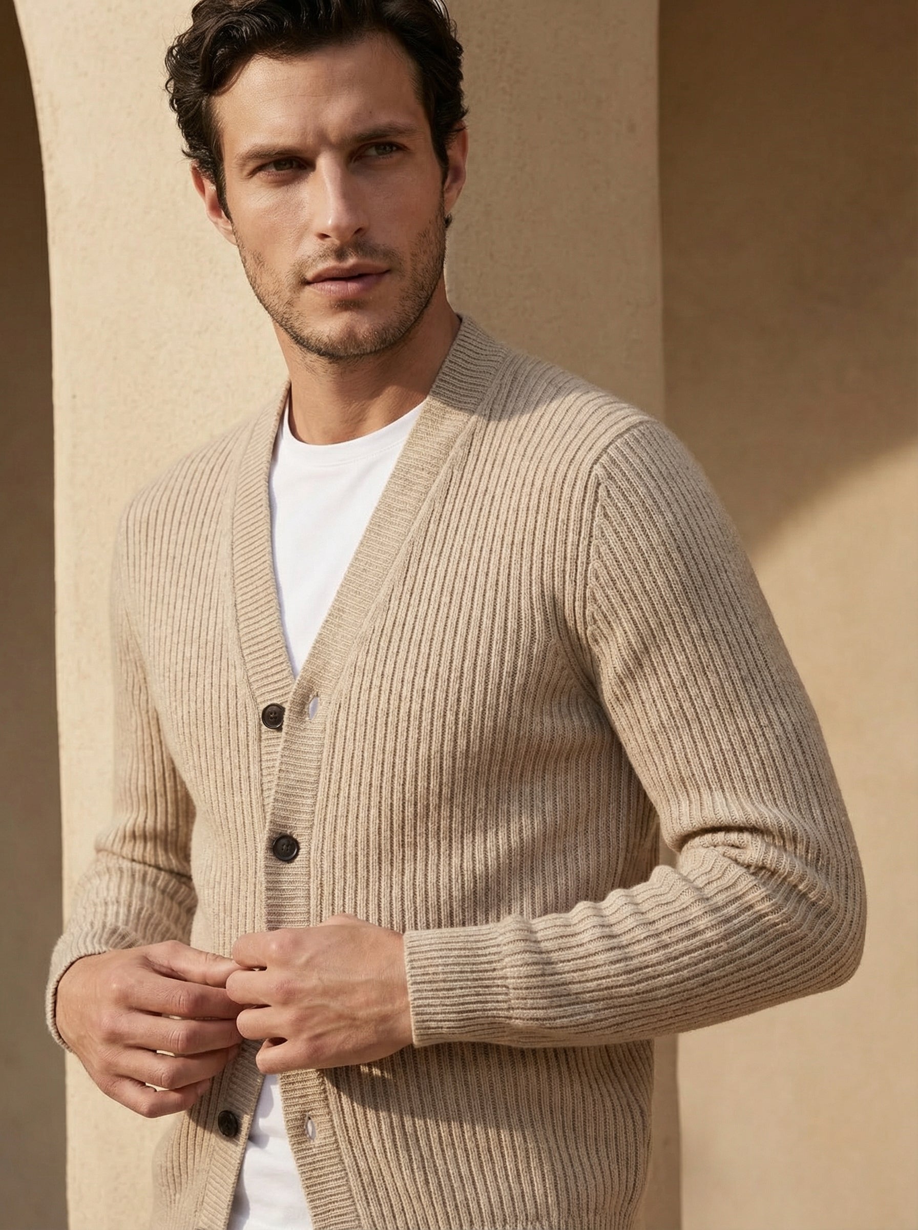 Man wearing a beige cardigan over a white shirt against a beige wall