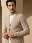 Man wearing a beige cardigan over a white shirt against a beige wall