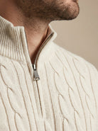 Close-up of a person wearing a cream cable knit sweater with a zipper.
