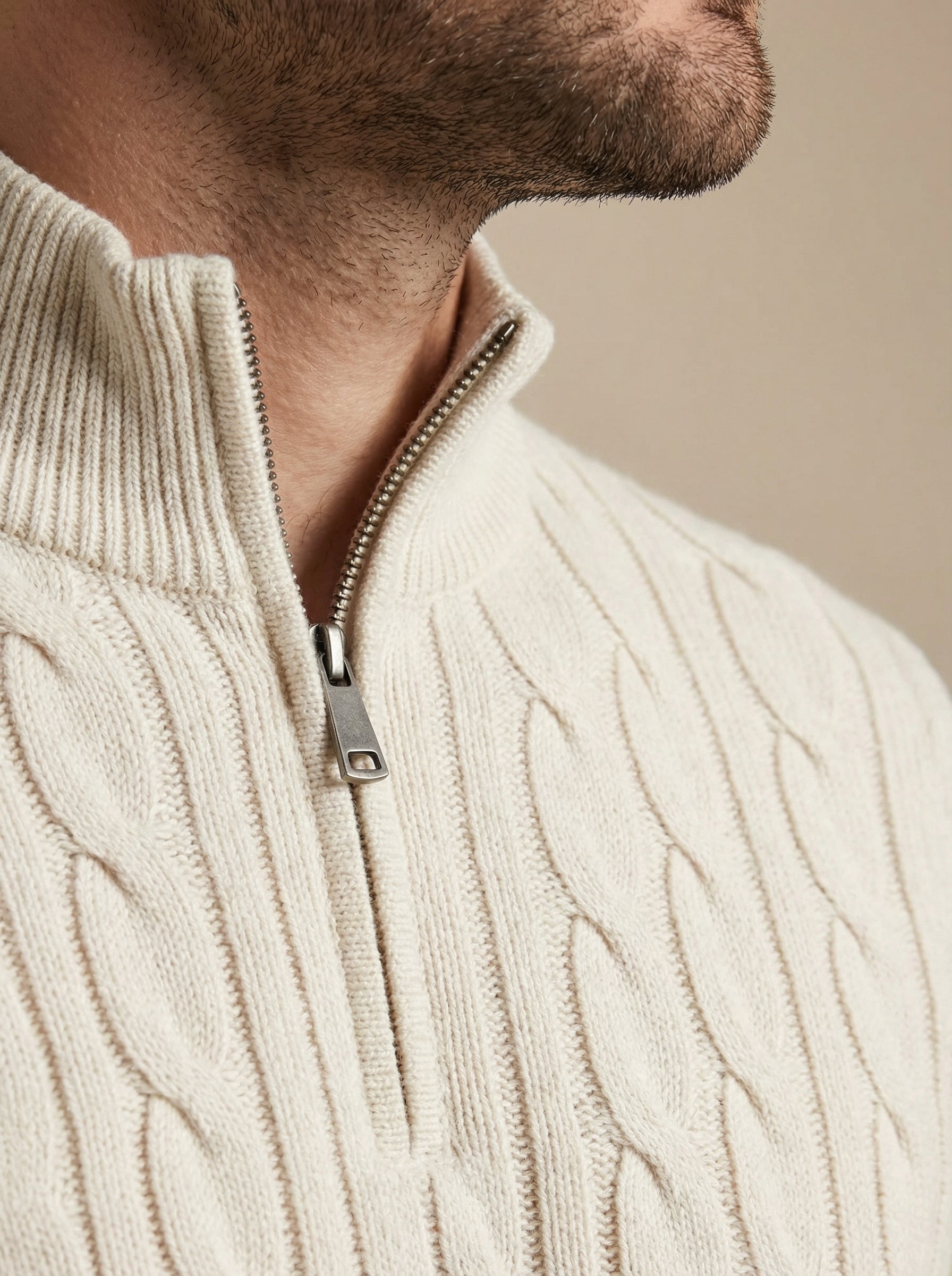 Close-up of a person wearing a cream cable knit sweater with a zipper.