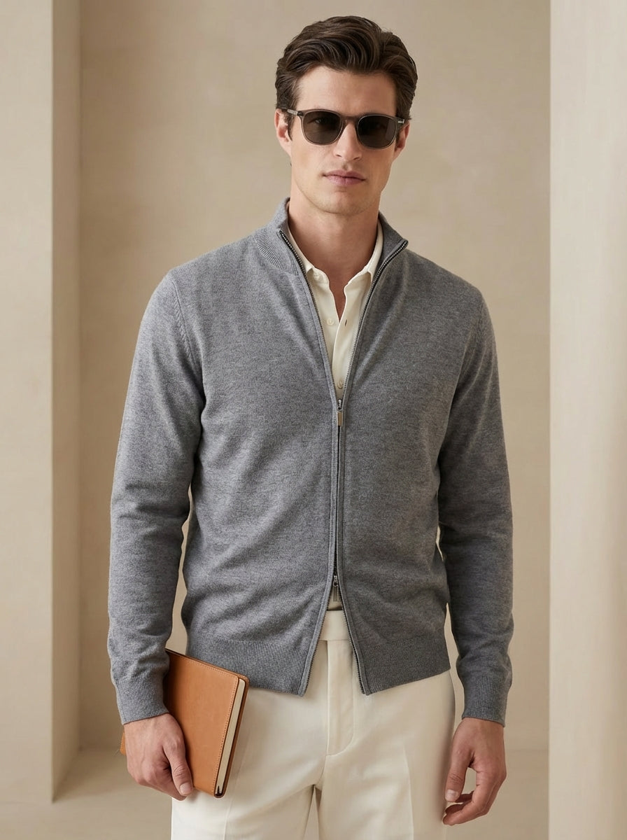 Man wearing a gray zip-up sweater over a white shirt, holding a brown leather folder against a beige background.