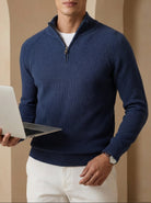 Man in a blue sweater holding a laptop against a beige archway background