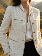 Woman wearing a cream-colored blazer with gold buttons in a mountainous landscape