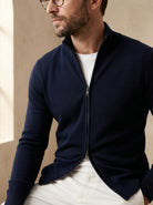 Man wearing a navy blue zip-up sweater over a white shirt against a beige background
