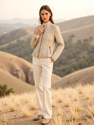 Woman in beige quilted jacket and pants standing in a desert landscape with mountains in the background.