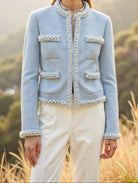 Woman wearing a light blue jacket with white pants standing in a scenic outdoor setting.