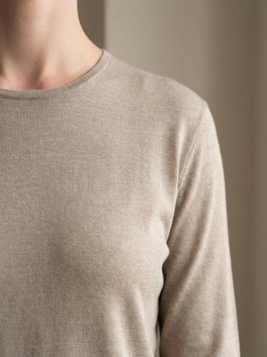 Close-up of a person wearing a beige long-sleeve shirt against a neutral background