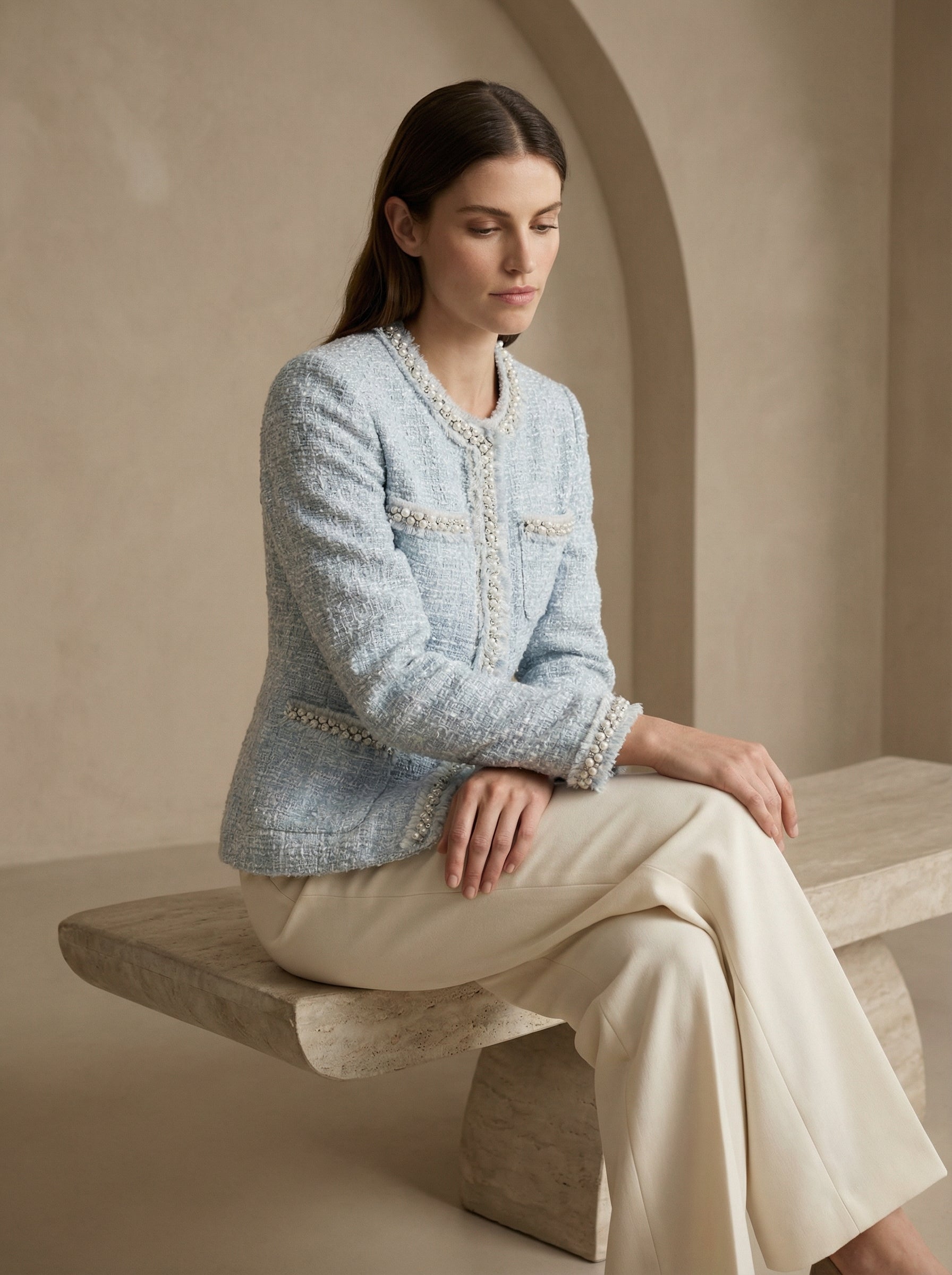 Woman wearing a light blue textured jacket with white trim sitting on a stone bench.