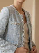 Woman wearing a light blue tweed jacket with pearl embellishments in an elegant setting.