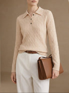 Woman wearing a beige ribbed sweater and white pants, holding a brown leather bag against a beige background.