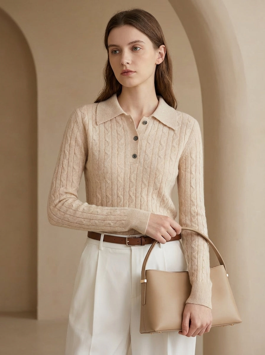 Woman wearing a beige cable knit sweater holding a matching handbag in an archway.