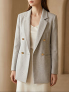 Woman wearing a gray blazer with gold buttons against a beige background, featuring the brand 'BLENIN'.