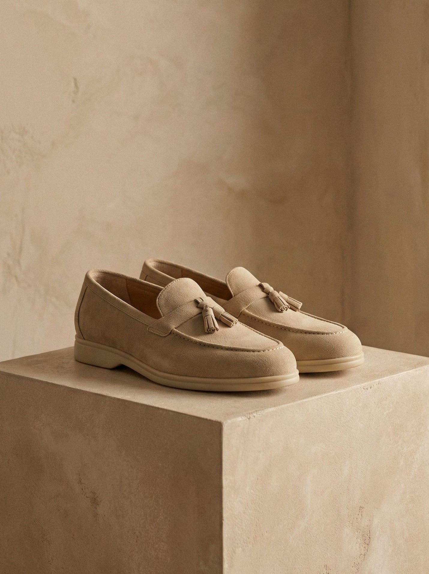 Pair of beige loafers with tassels on a beige platform against a neutral background