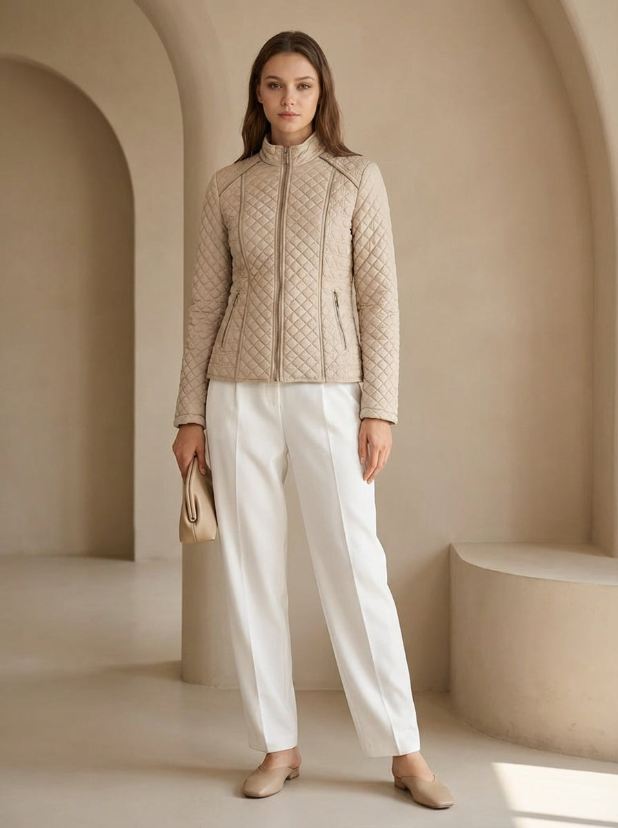 Woman wearing a beige quilted jacket and white pants in a neutral setting