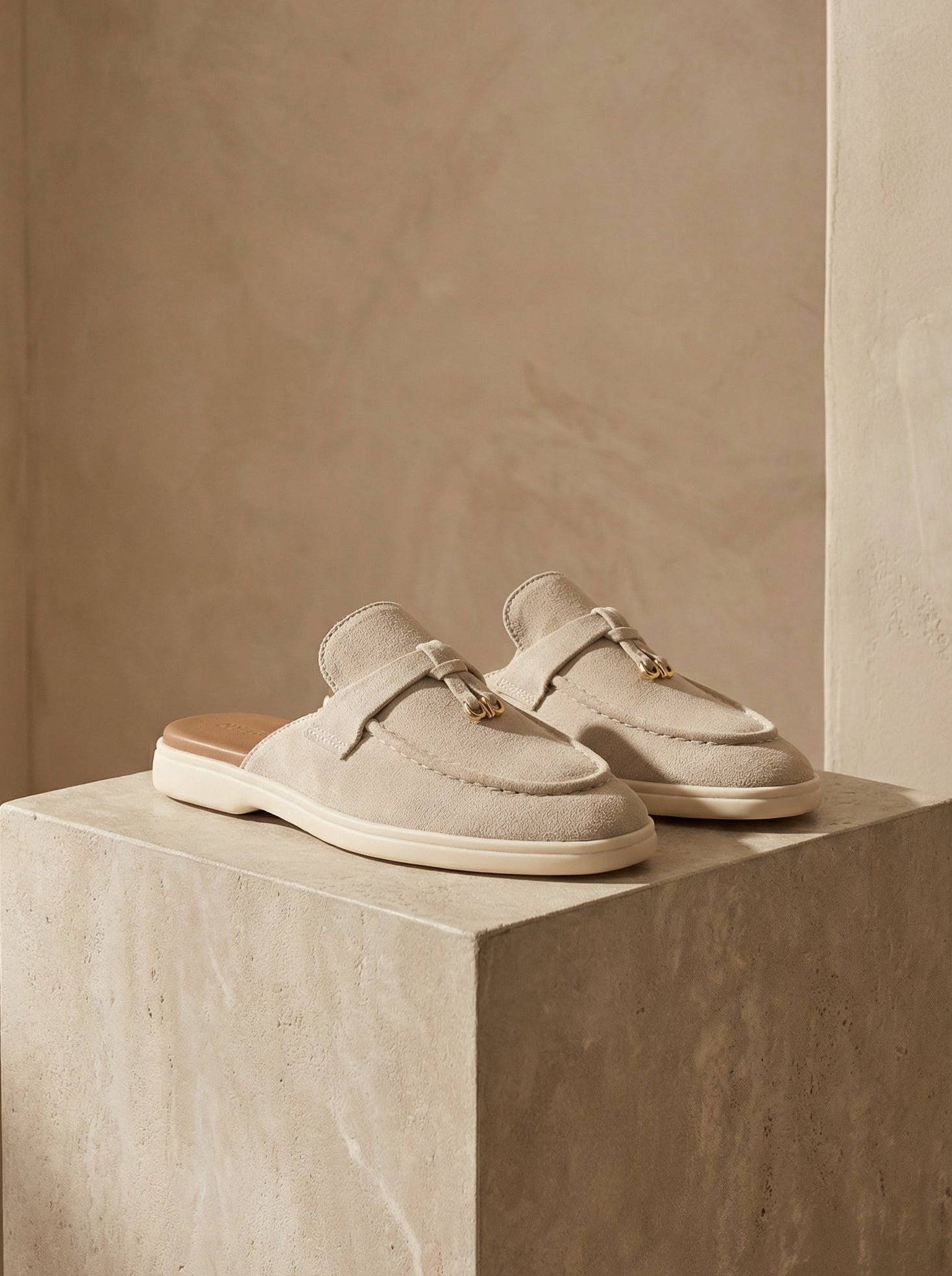 Pair of light gray loafers on a beige pedestal against a neutral background