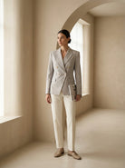Woman in a gray blazer and white pants standing in a softly lit room.